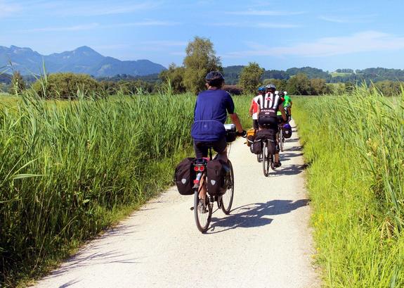 Fahrradfahrer auf einem Weg, der durch grüne Wiesen führt, blauer Himmel im Hintergrund