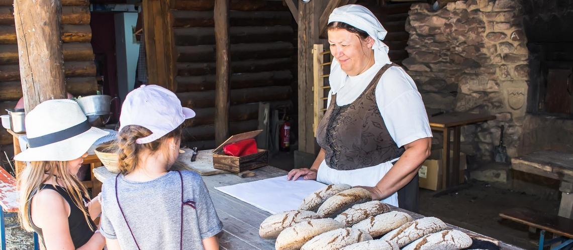 Zwei Kinder kaufen Brot an der Theke der Bäckerei im Handwerkerdorf